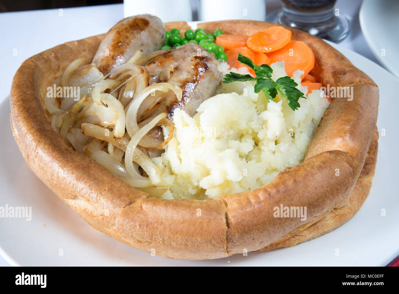 An English pub/restaurant lunch of giant Yorkshire pudding filled with Sausage and onions, creamed potato, vichy carrots, garden peas and gravy Stock Photo