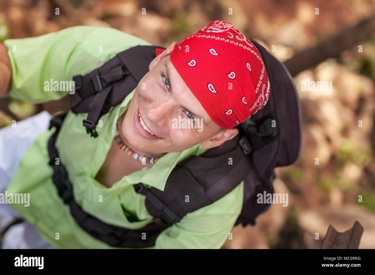 View from top on young man with green shirt and red bandana looking up and  smiling, wearing backpack Stock Photo - Alamy