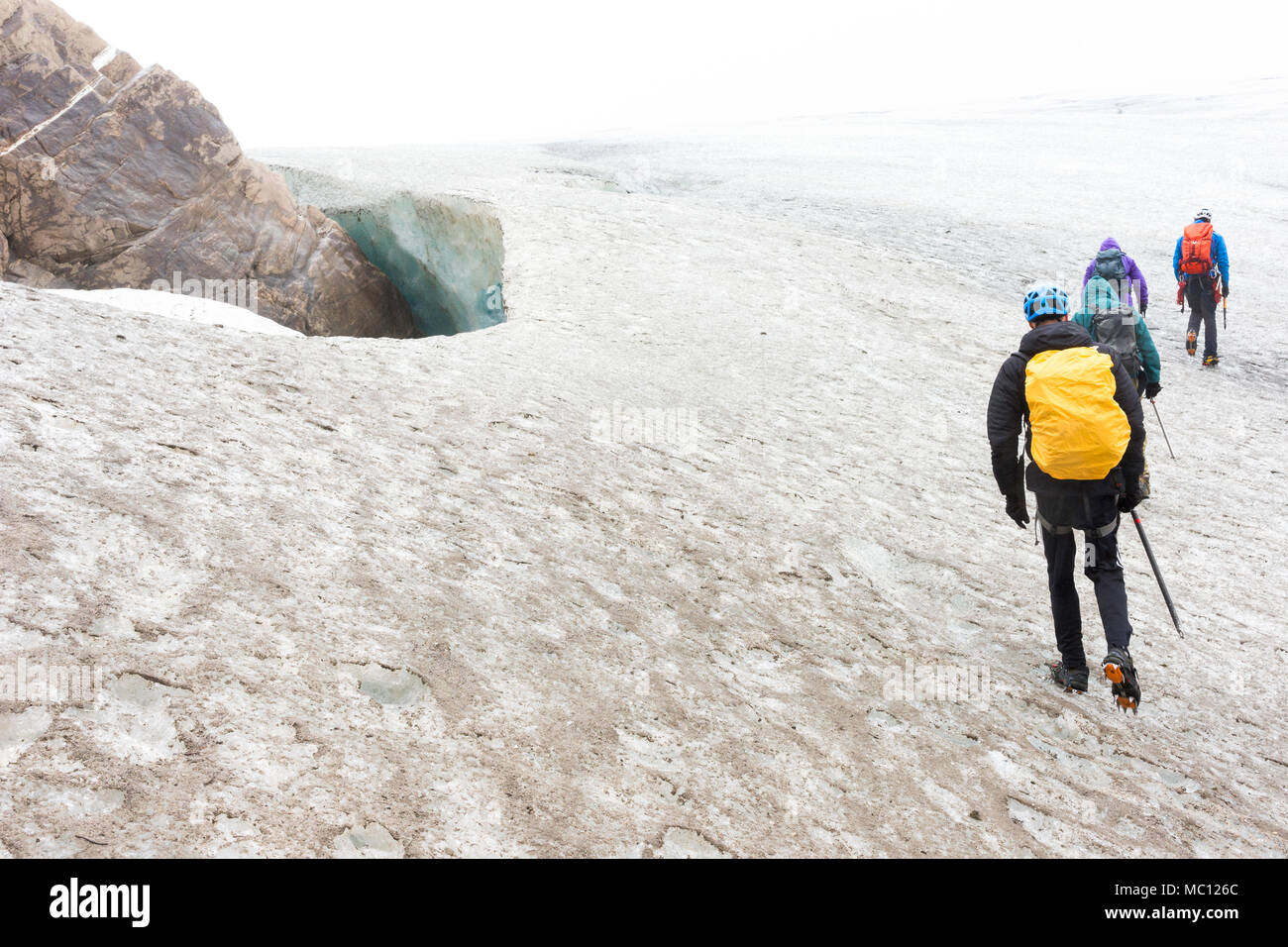 Four people trek across an icy glacier past a dangerous crevasse during a tourist adventure, Juneau Icefield, Juneau, Alaska, USA Stock Photo