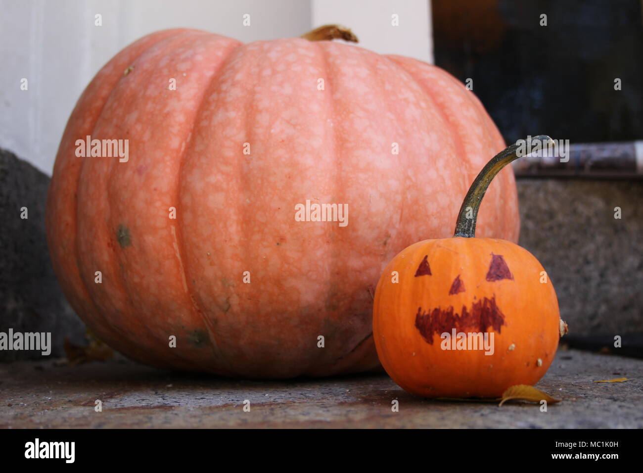 A perfect large light orange pumpkin on a doorstep with a small pumpkin with a face drawn on it with sharpie seen on Beacon Street, Boston, in October. Stock Photo
