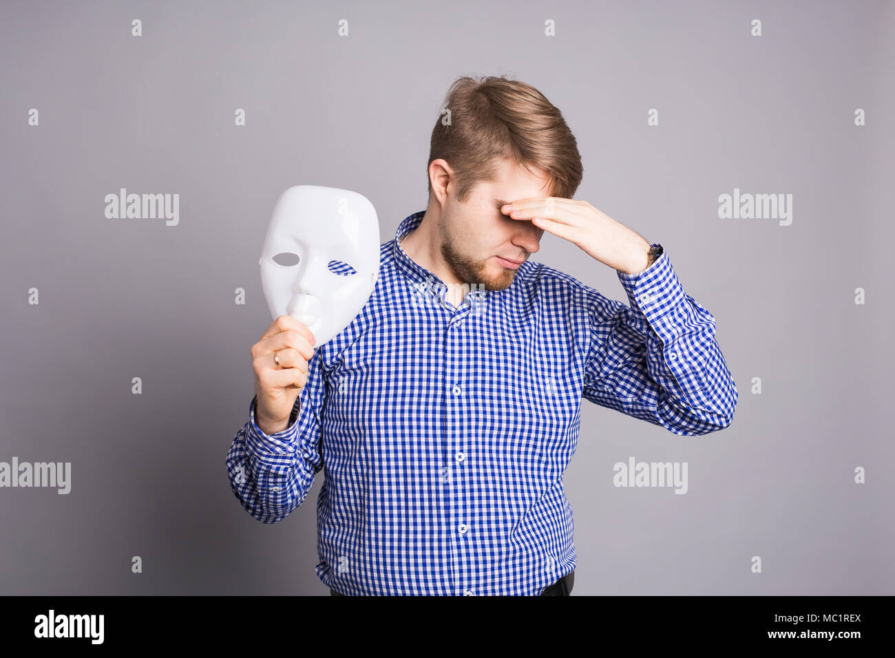 Sad man taking off plain white mask revealing face, gray background ...