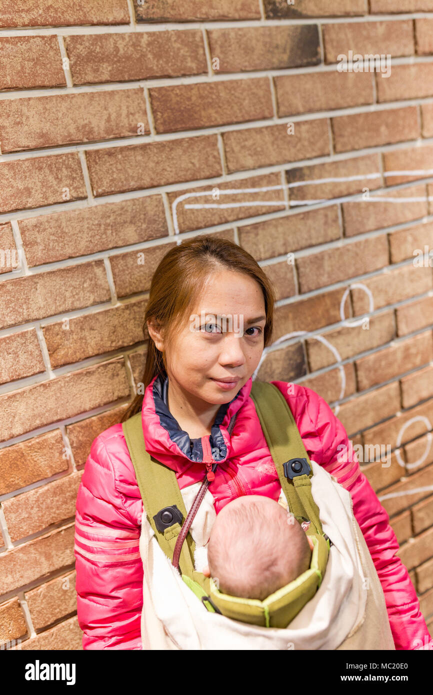 Young mother carrying baby in baby carrier standing next to brick wall Stock Photo Alamy