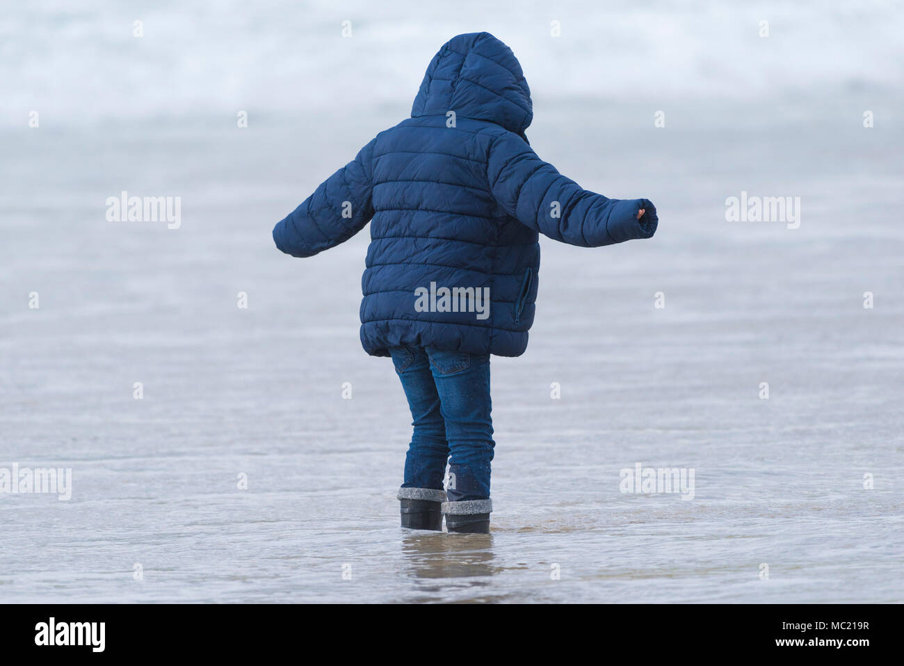 A young boy wearing a hooded jacket standing in the sea. Stock Photo