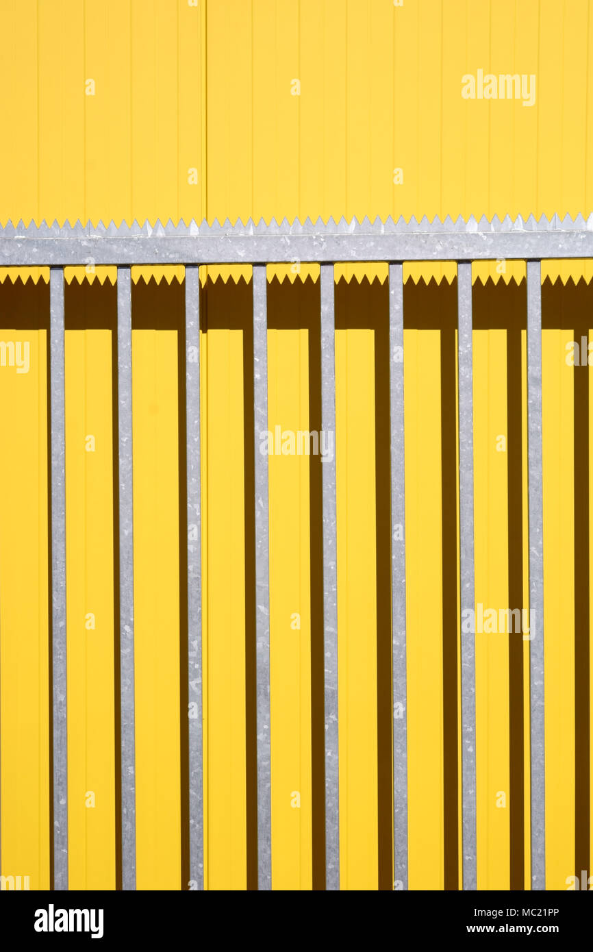 The side view of a color intensive corrugated iron wall of a shopping center with a leaning pointed serrated part of an open entrance gate. Stock Photo