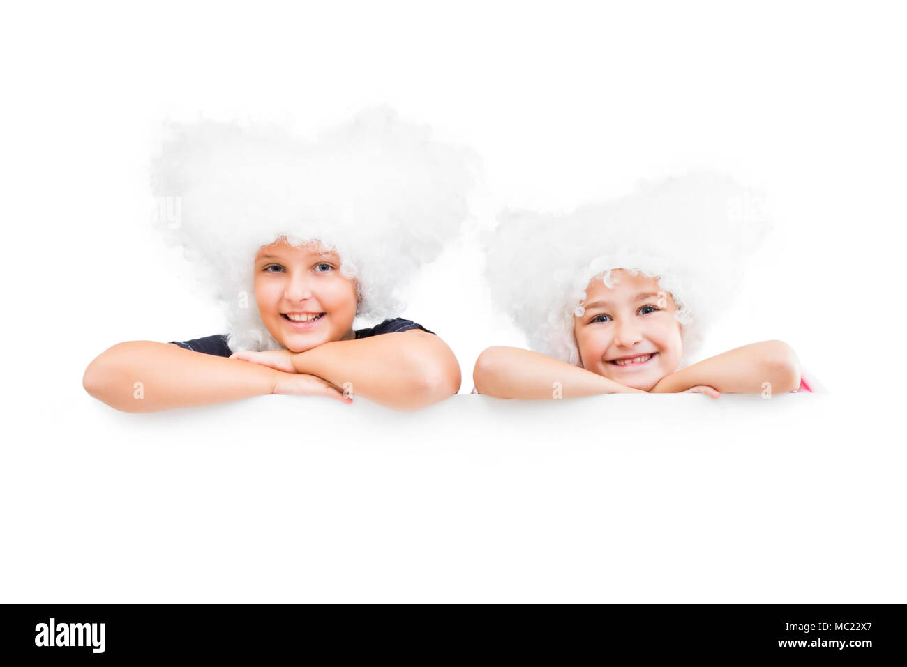 Smiling happy two young girls in white wigs  look out from the empty banner. Stock Photo