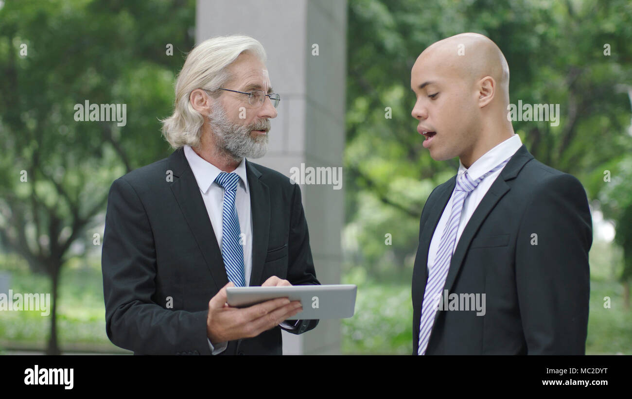 caucasian and latino corporate executives discussing business using digital tablet. Stock Photo