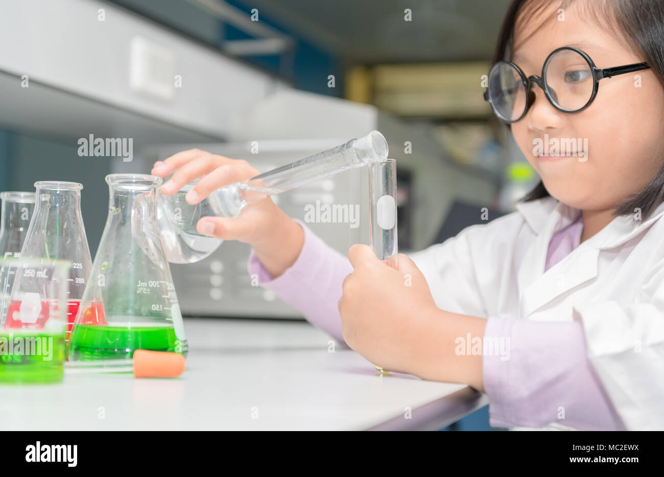 Happy scientist girl in lab coat making experiment with test tube in ...