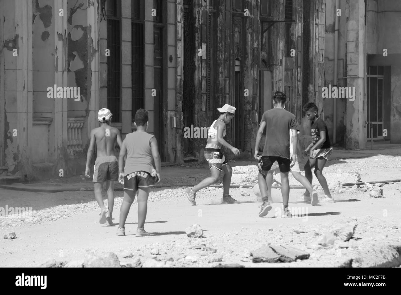 Black and white photograph of Cuban children playing soccer in the streets of a dirtied street in Havana, Cuba Stock Photo