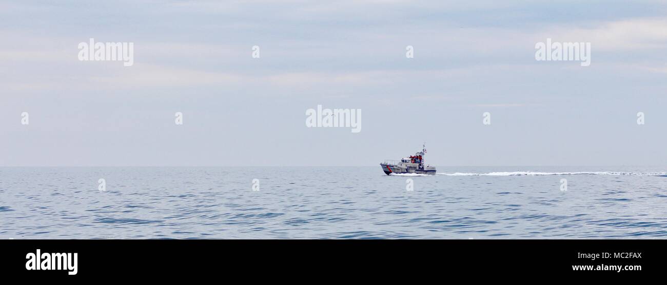 A lone fishing boat sailing the wide open ocean in Gloucester off the coast with a light blue sky with a few clouds. Stock Photo