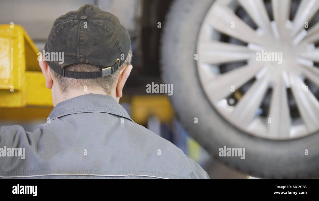 Rear view of mechanic near car on the lift in a service station Stock