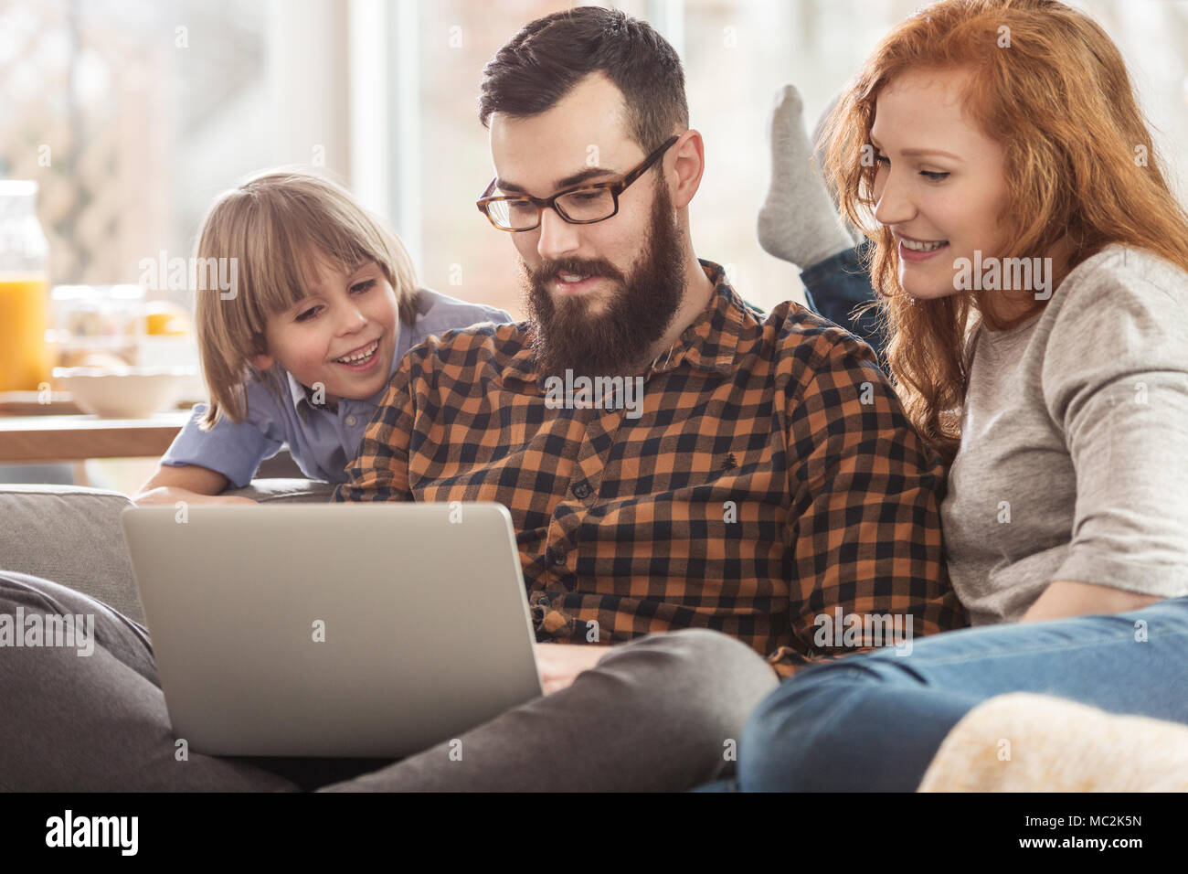 Happy family watching photos together on a laptop while sitting on a couch Stock Photo