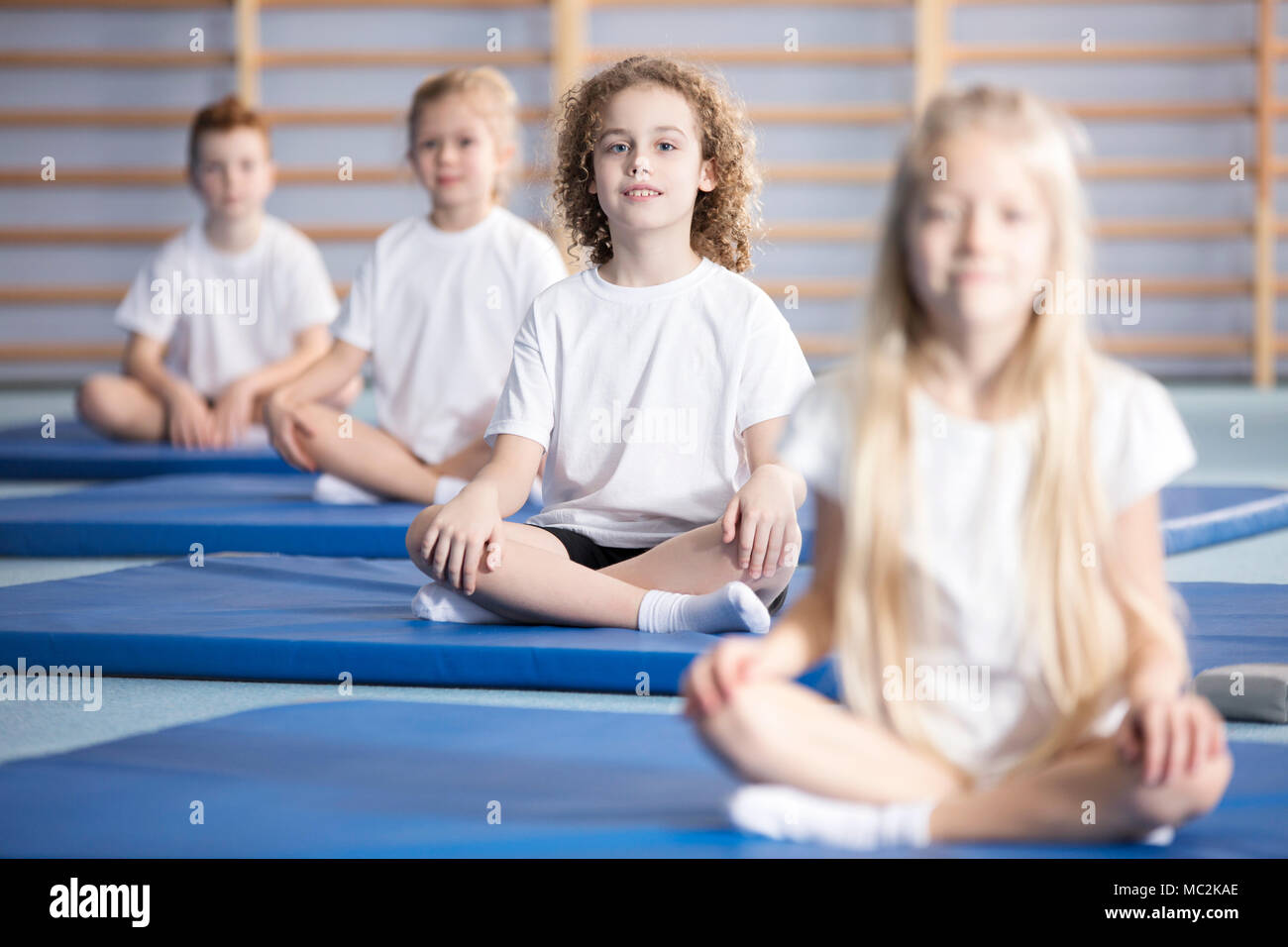 Smiling boy and friends sitting on blue mats during a corrective gymnastics class Stock Photo
