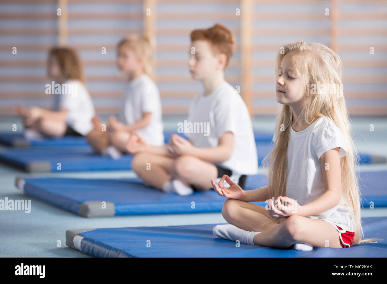 Group of children sitting in lotus pose on blue mats during a yoga class Stock Photo