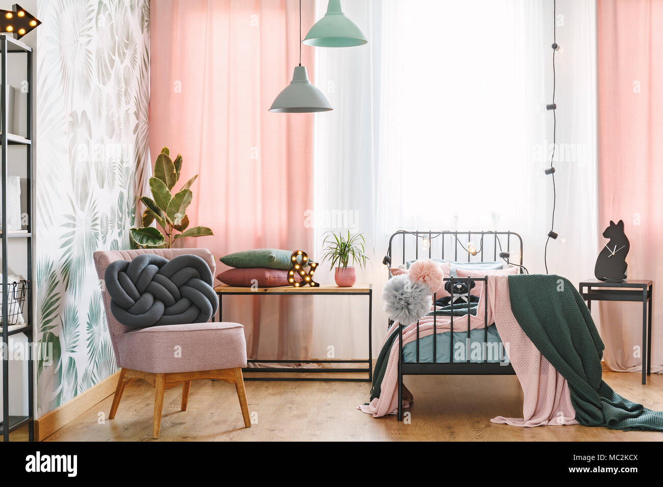Pink chair with handmade, grey knot cushion placed in bright bedroom