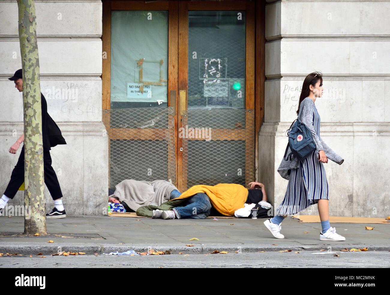 London, England, UK. Two homeless people sleeping in a doorway in St Martin's Place, near Trafalgar Square - PEOPLE WALKING PAST Stock Photo