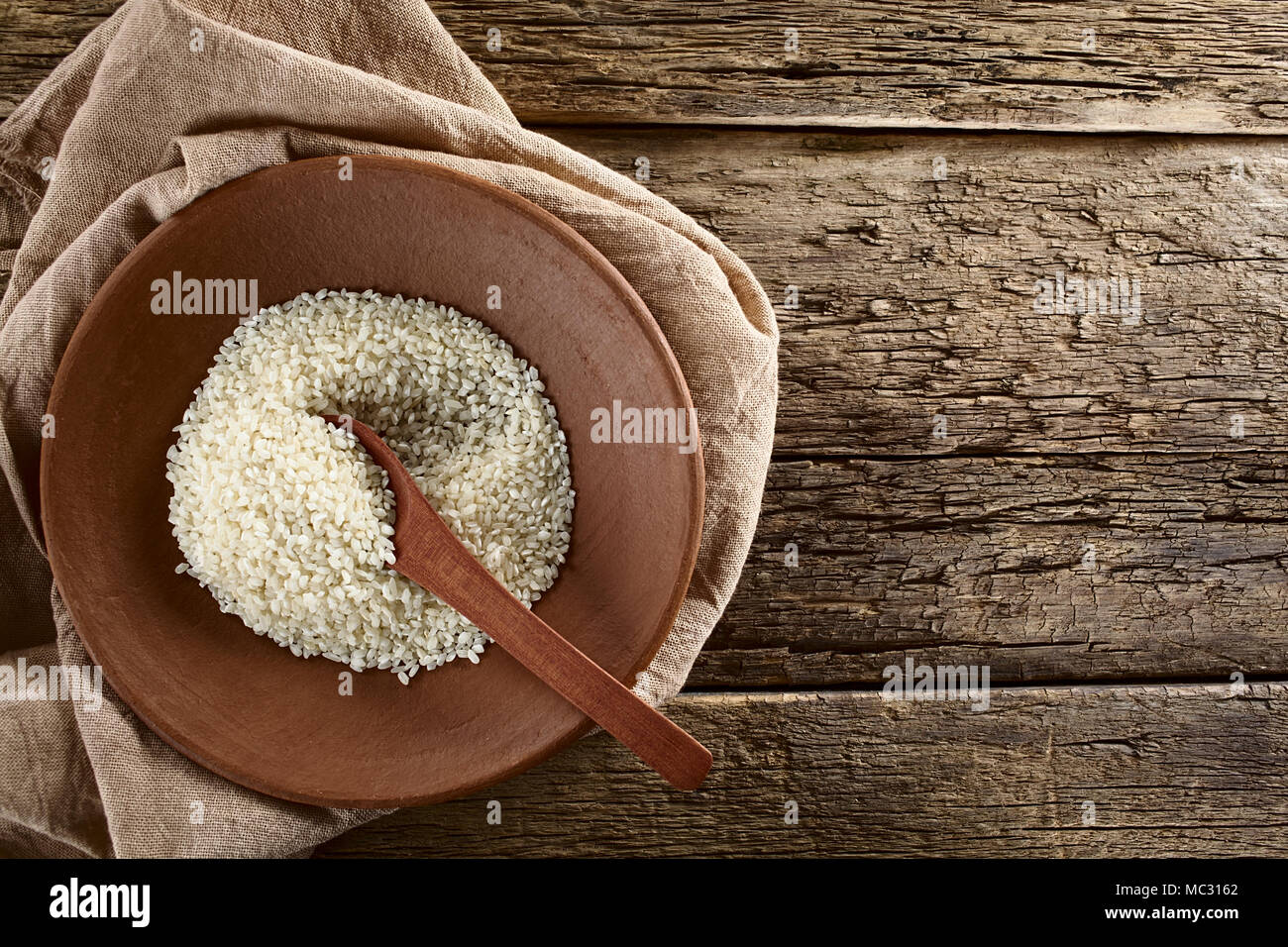 Raw arborio risotto shortgrain rice on clay plate with wooden spoon
