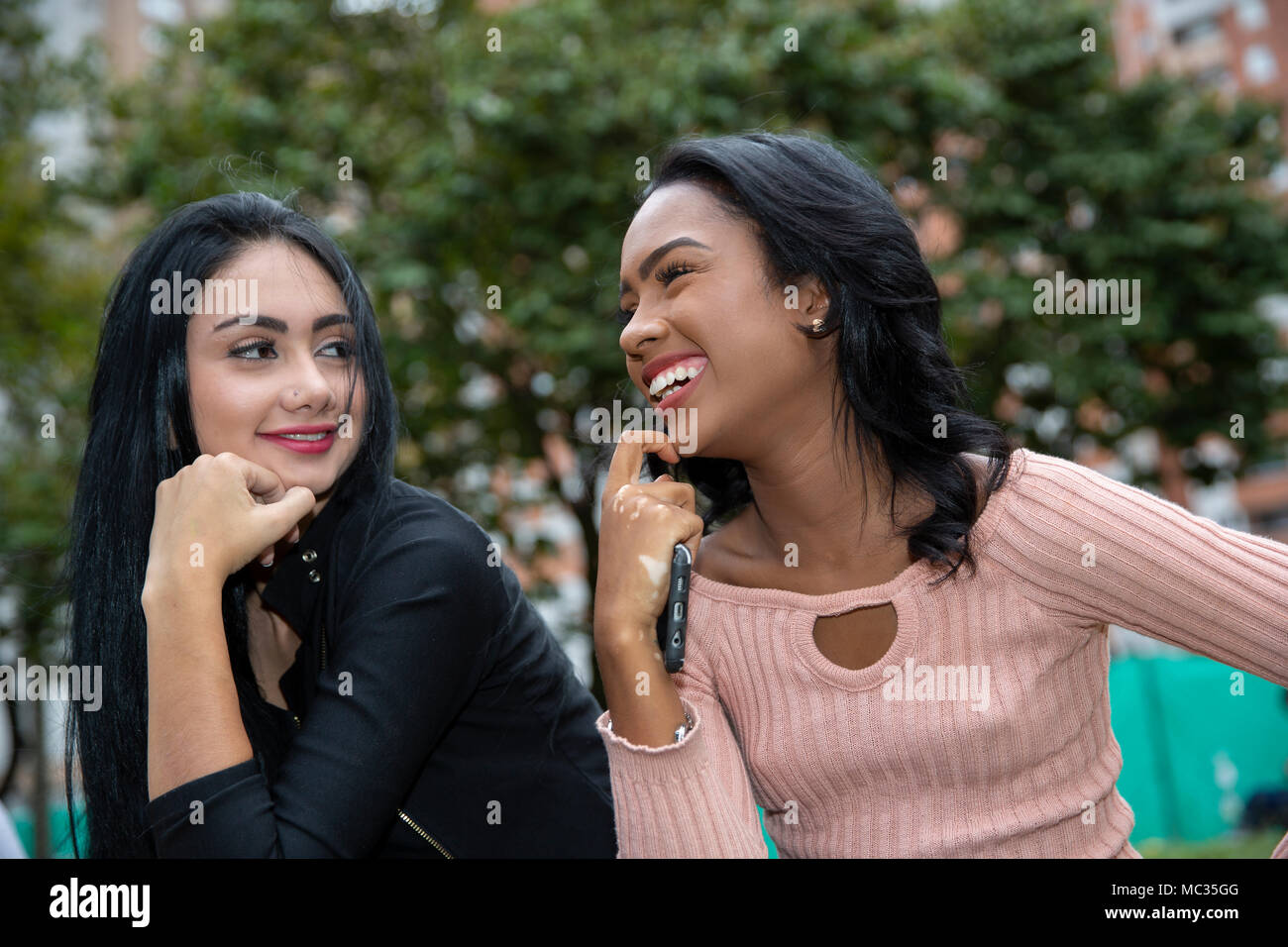 Young female friends smiling while looking at each other in park Stock Photo