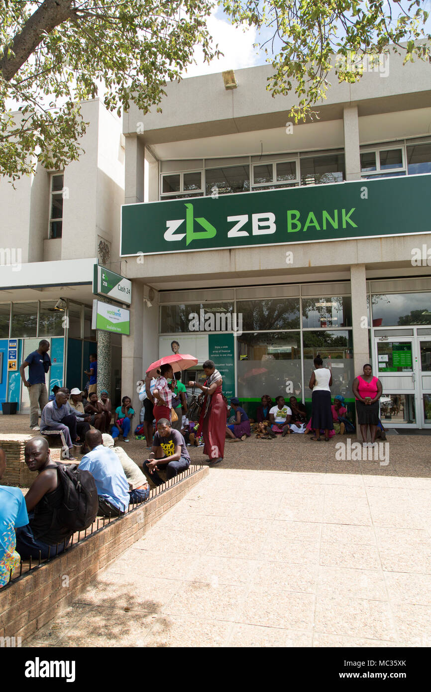 People queuing outside of ZB Bank at Victoria Falls in Zimbabwe. The people await an opportunity to wishdraw cash. Stock Photo