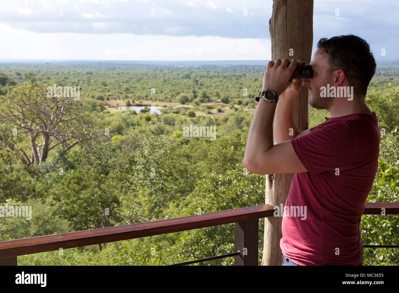 A man with binoculars looks into Victoria Falls National Park seen from Victoria Falls Safari Lodge in Zimbabwe. Stock Photo