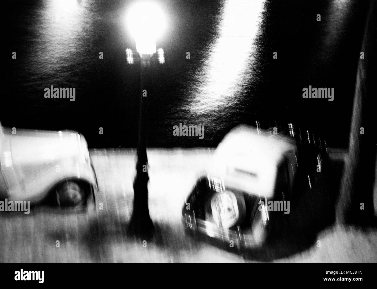 Abstract riverside view of automobiles under a street lamp in France, ca. 1938. Stock Photo