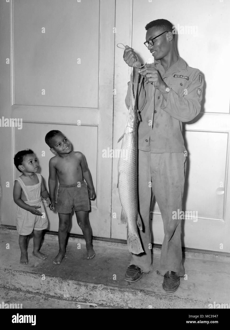 An US Army dad shows off the Alligator Gar he caught in the American South to his children, ca. 1961. Stock Photo