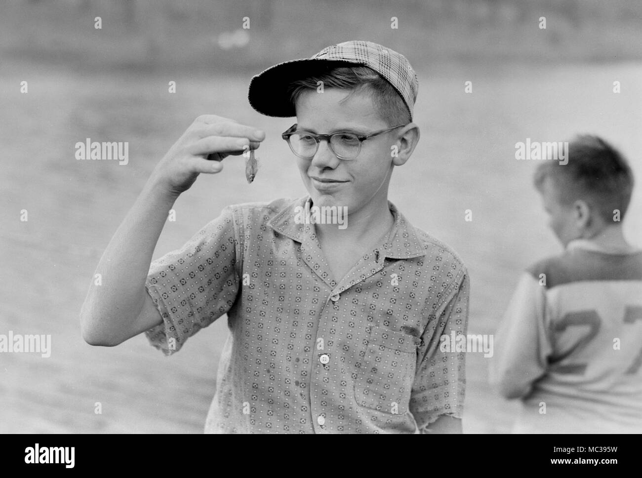 A young boy seems apprehensive about the size of his catch, ca. 1960. Stock Photo