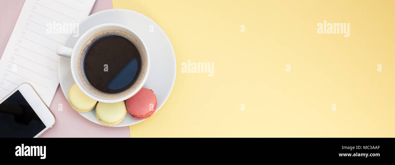 Creative flat lay photo of coffee cup with macaroons and a notepad with copy space on pink and yellow background minimal style Stock Photo