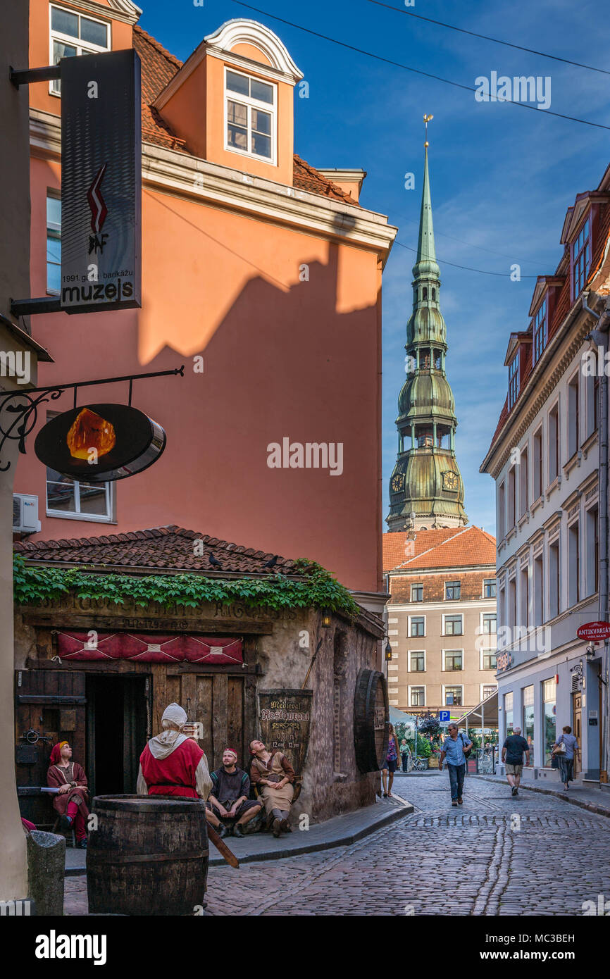 A restaurant with staff dressed up in faux traditional wear, with Rīgas Sv. Pētera baznīca (St Peter's Church) in the background, in Riga (Latvia). Stock Photo