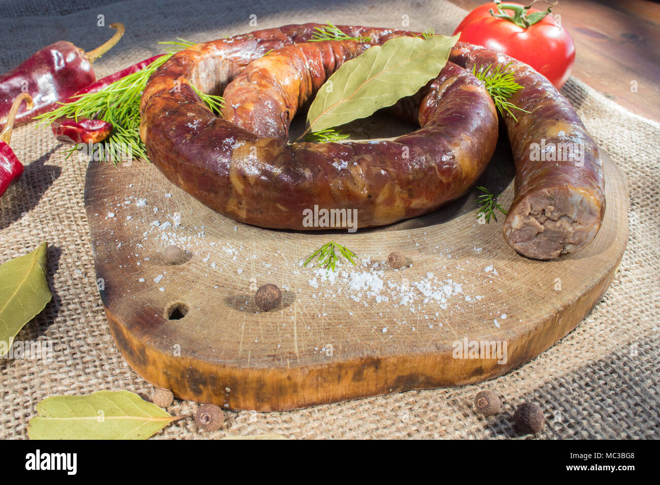 A ring of cooked sausage on the grill. Next to it is a tomato Stock Photo