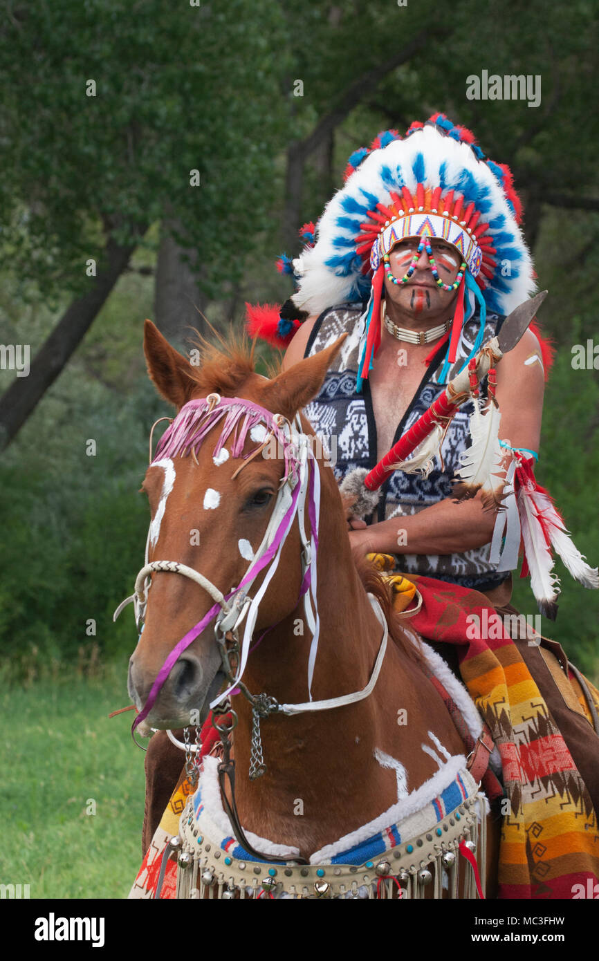 Warrior in Comanche clothing riding chestnut horse decorated in war ...