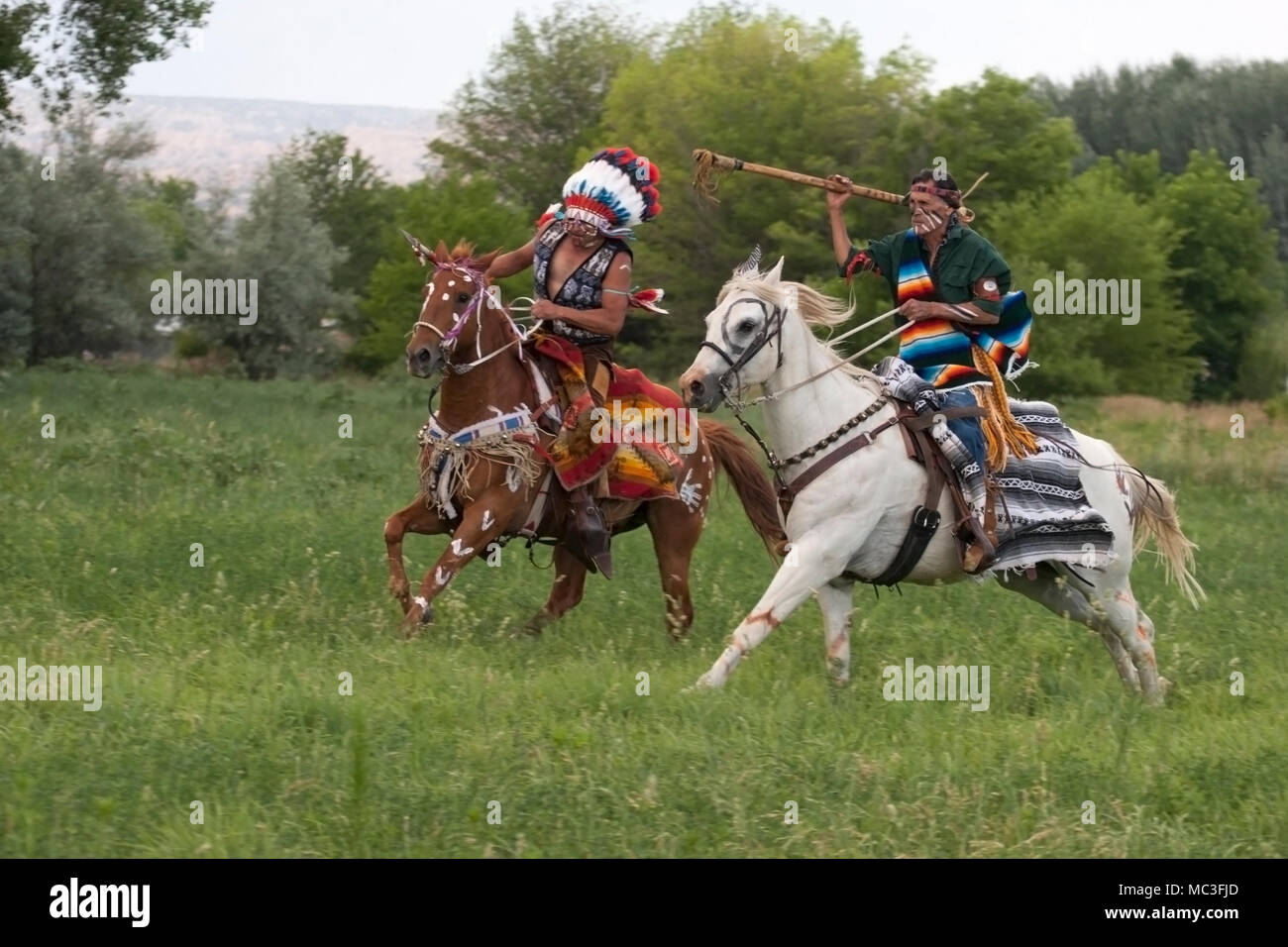 Warriors in Comanche clothing galloping horses through meadow Stock Photo