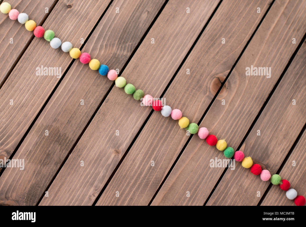 Wooden backround with small colorfull textile pompon decoration. Bright bobs Stock Photo