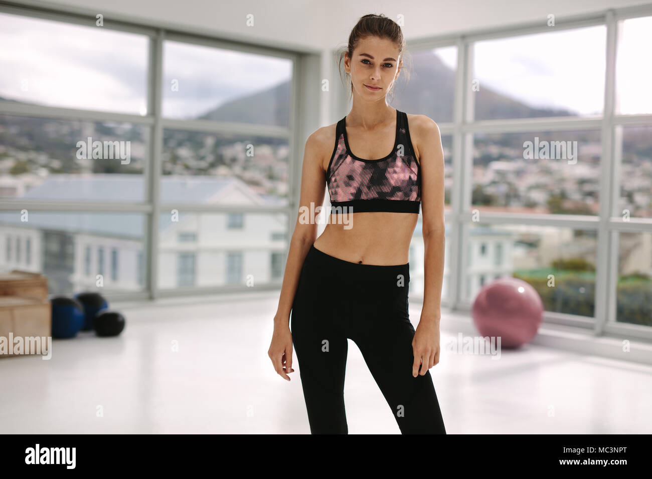 Portrait of woman with slim body standing at fitness studio. Beautiful female in sportswear standing in gym and looking at camera. Stock Photo