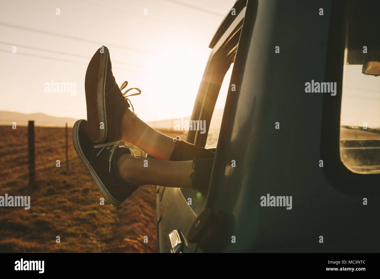 Close up of legs of a relaxing woman hanging out from car on a highway ...