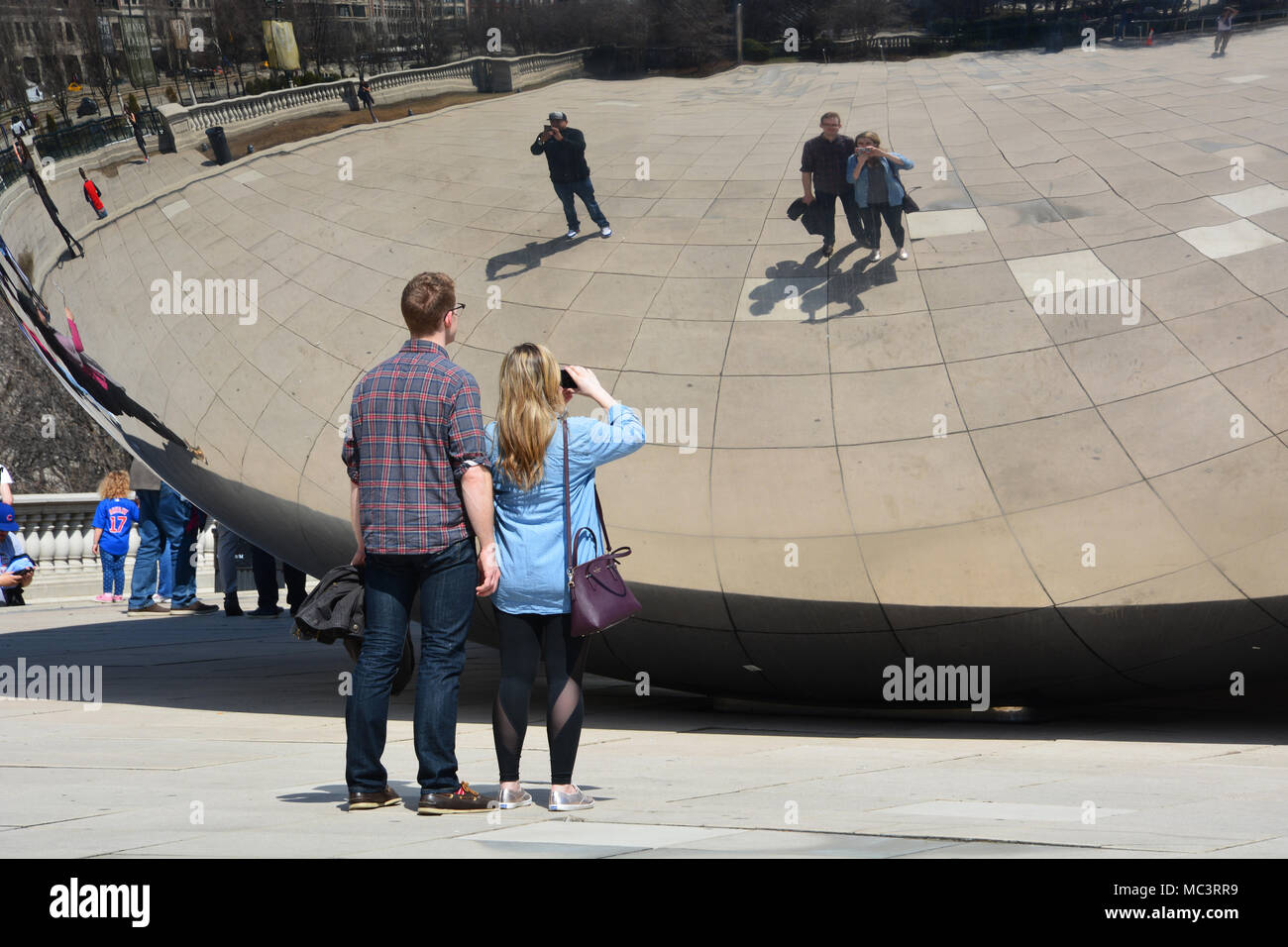 A young couple pose for selfies with Chicago's "Bean" in Millennium Park on a warm spring day. Stock Photo