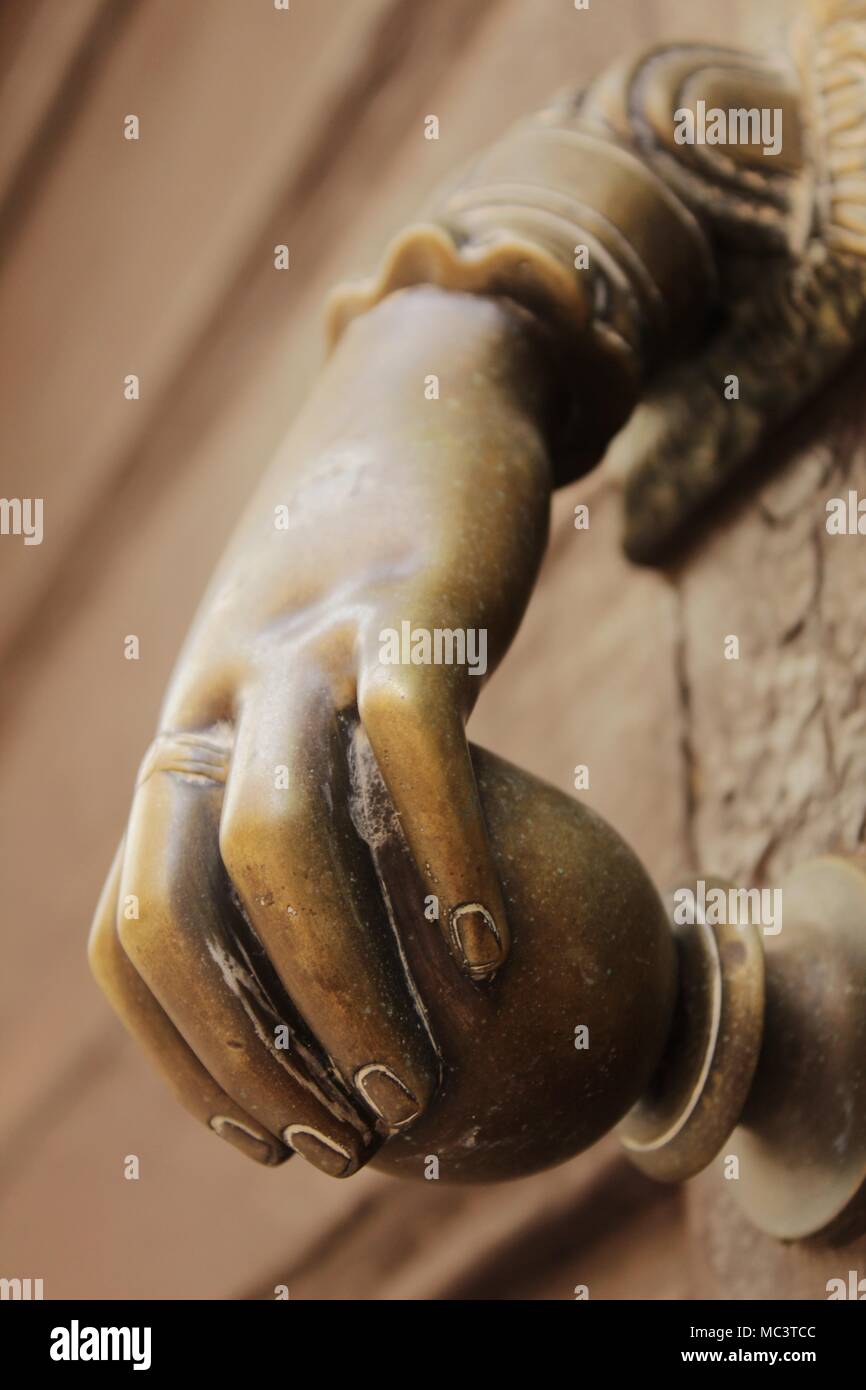 Golden Doorknocker With Hand Shape On Old Brown Wooden Door In