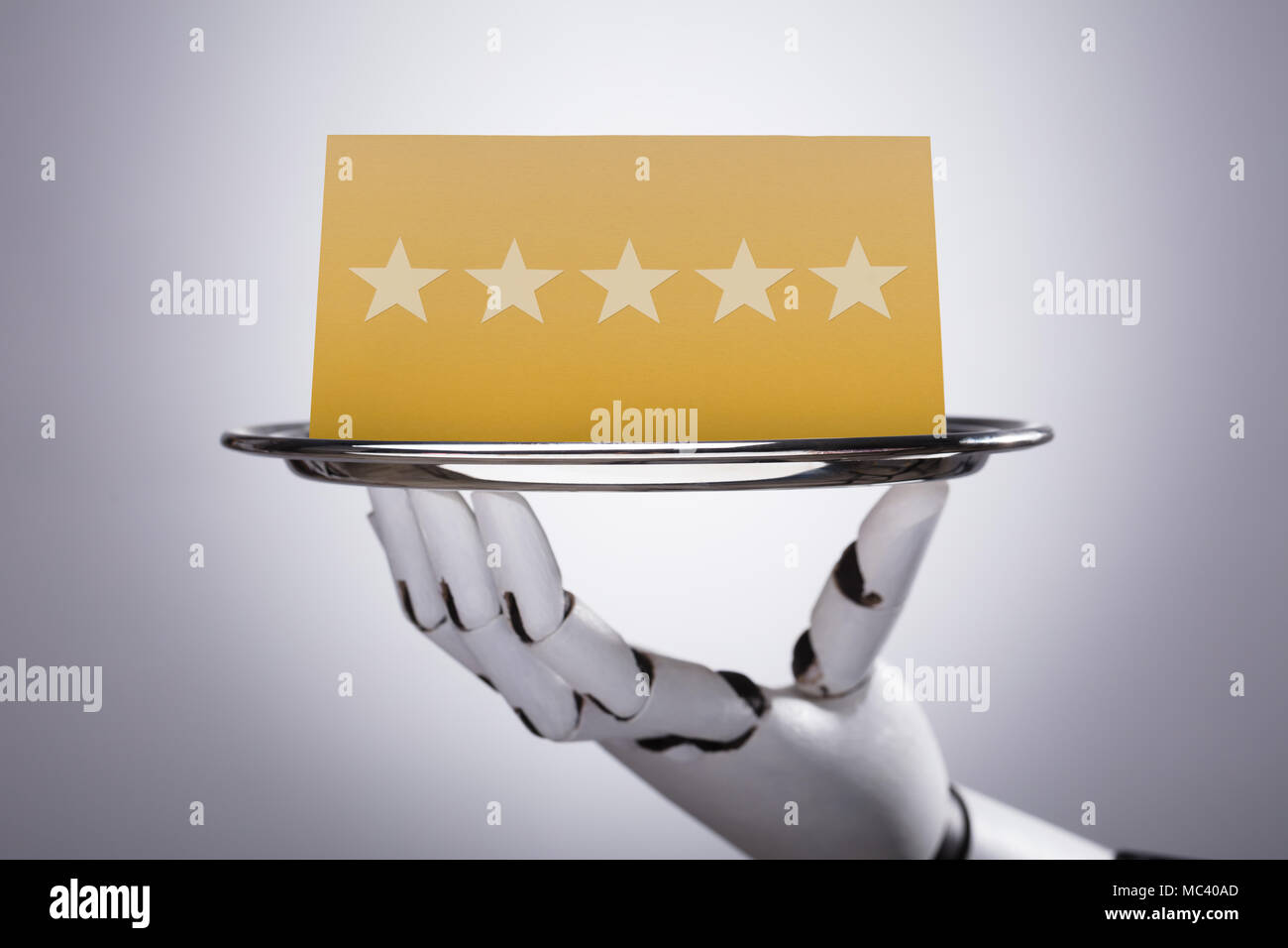 Close-up Of A Robotic Hand Holding Plate With Star Rating On Grey Background Stock Photo