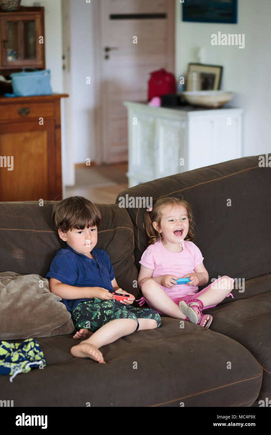 Kids boy and girl playing video game sitting on sofa at home. Children playing together Stock Photo