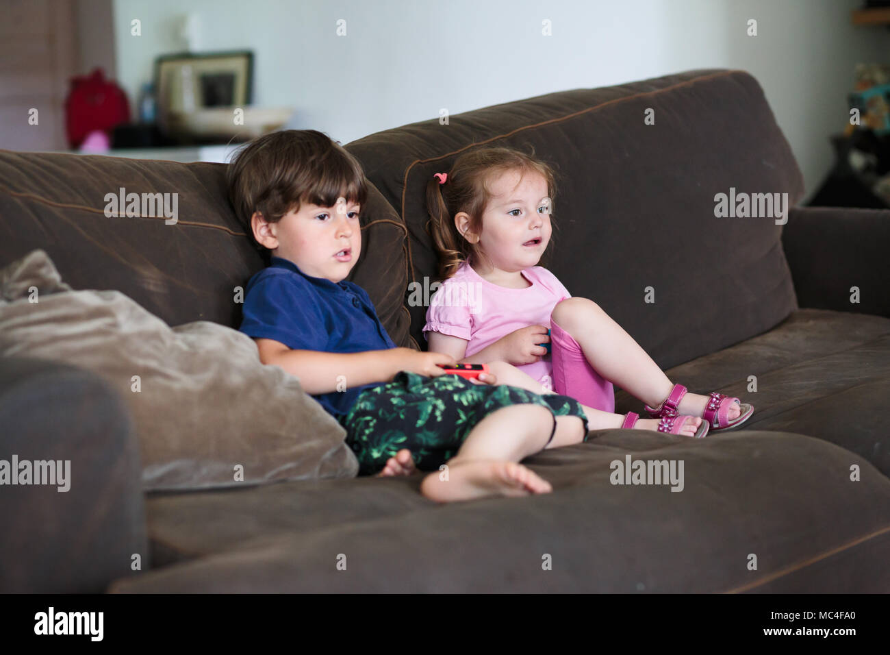 Kids boy and girl playing video game sitting on sofa at home. Children playing together Stock Photo