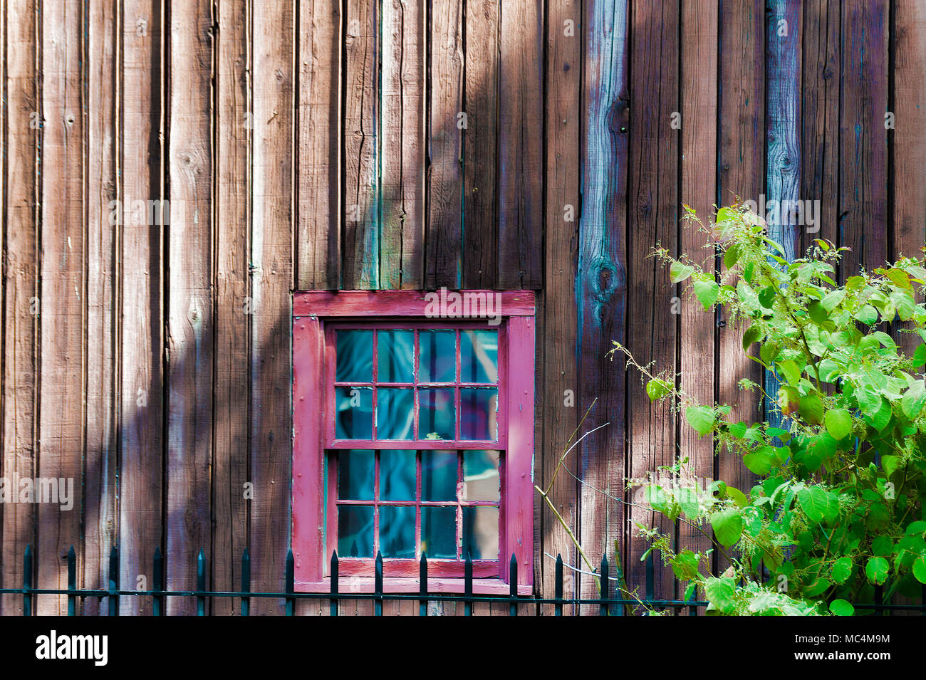 An old wooden building with a red framed window, sunlight casting shadows in this background image. Stock Photo