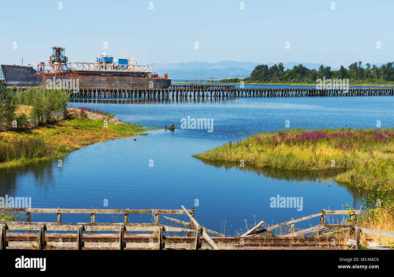 An old rusted out ship docked on the Columbia River near Astoria, Oregon, railroad tracks in the foreground Stock Photo