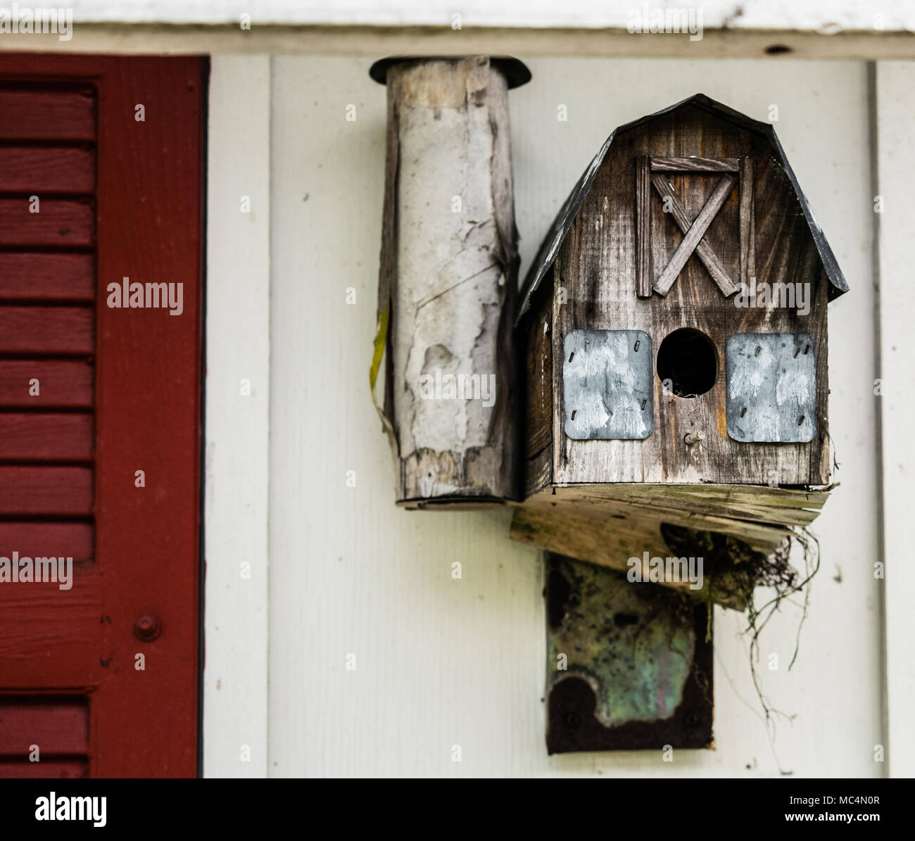 An aged birdhouse attached to a barn. Twigs from a nest inside the ...