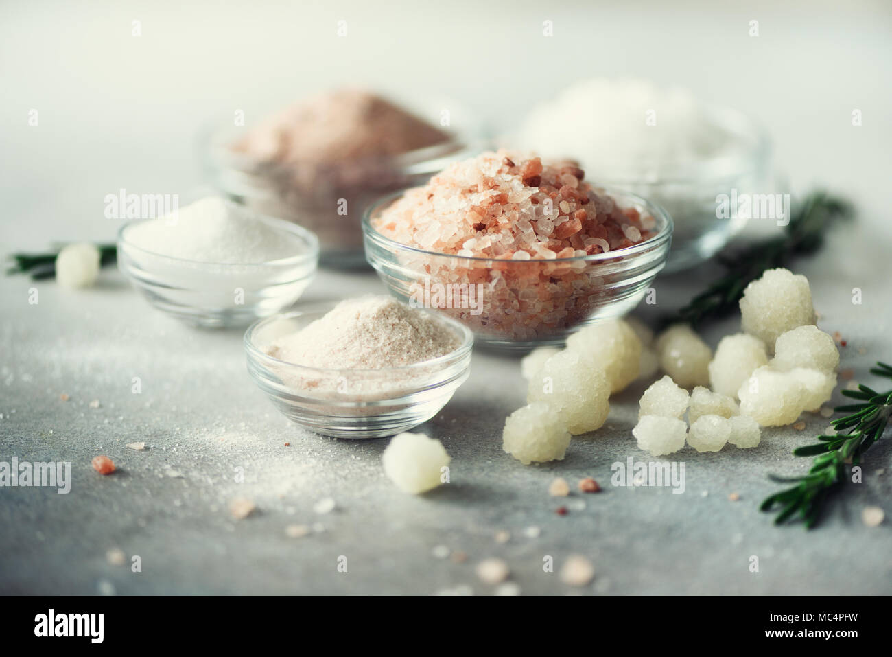 Mix of different salt types on grey concrete background. Sea salts, black and pink Himalayan salt crystals, powder, rosemary. Salt crystal balls from Dead sea. Copy space Stock Photo