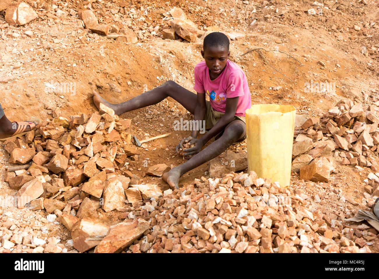 Lugazi, Uganda. June 18 2017. A Ugandan boy breaking rocks into small slabs for his foreman. Basically child labour. Stock Photo