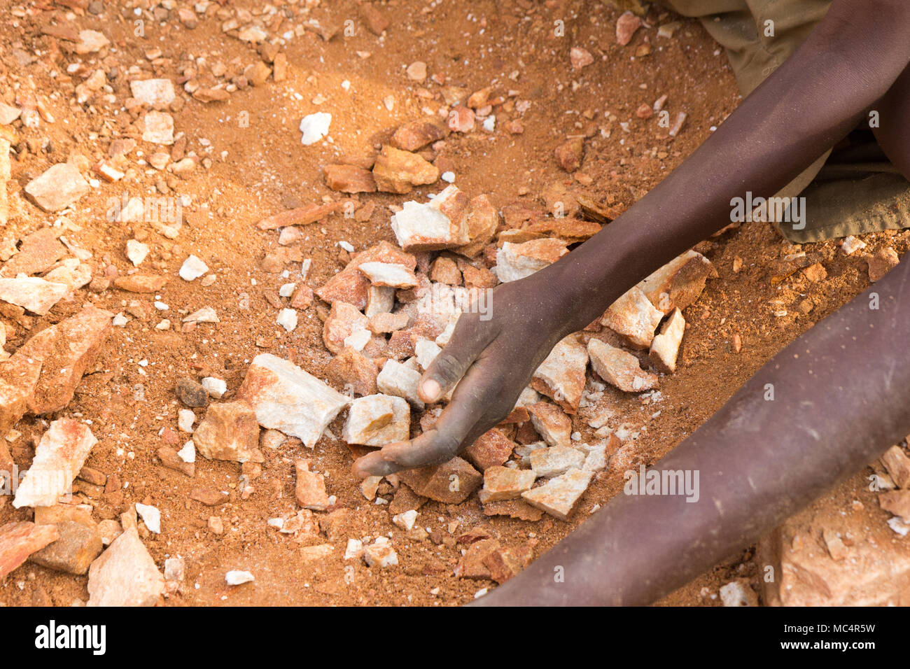 Ugandan child's hands breaking rocks into small slabs for his or her foreman. Shot in Uganda in June 2017. Stock Photo