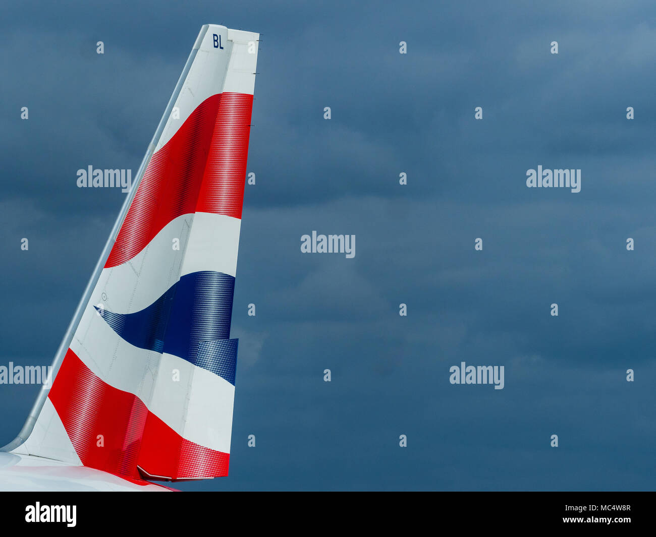 British Airways Tail Fin - Tail Fin of a BA Boeing 777 against dark clouds Stock Photo
