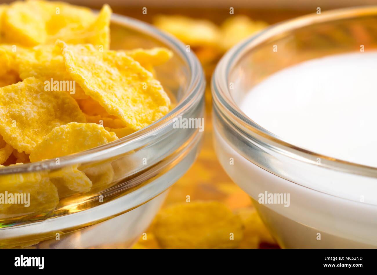 Ingredients for breakfast. Dry corn flakes and milk in a transparent cup close-up with blur. Stock Photo