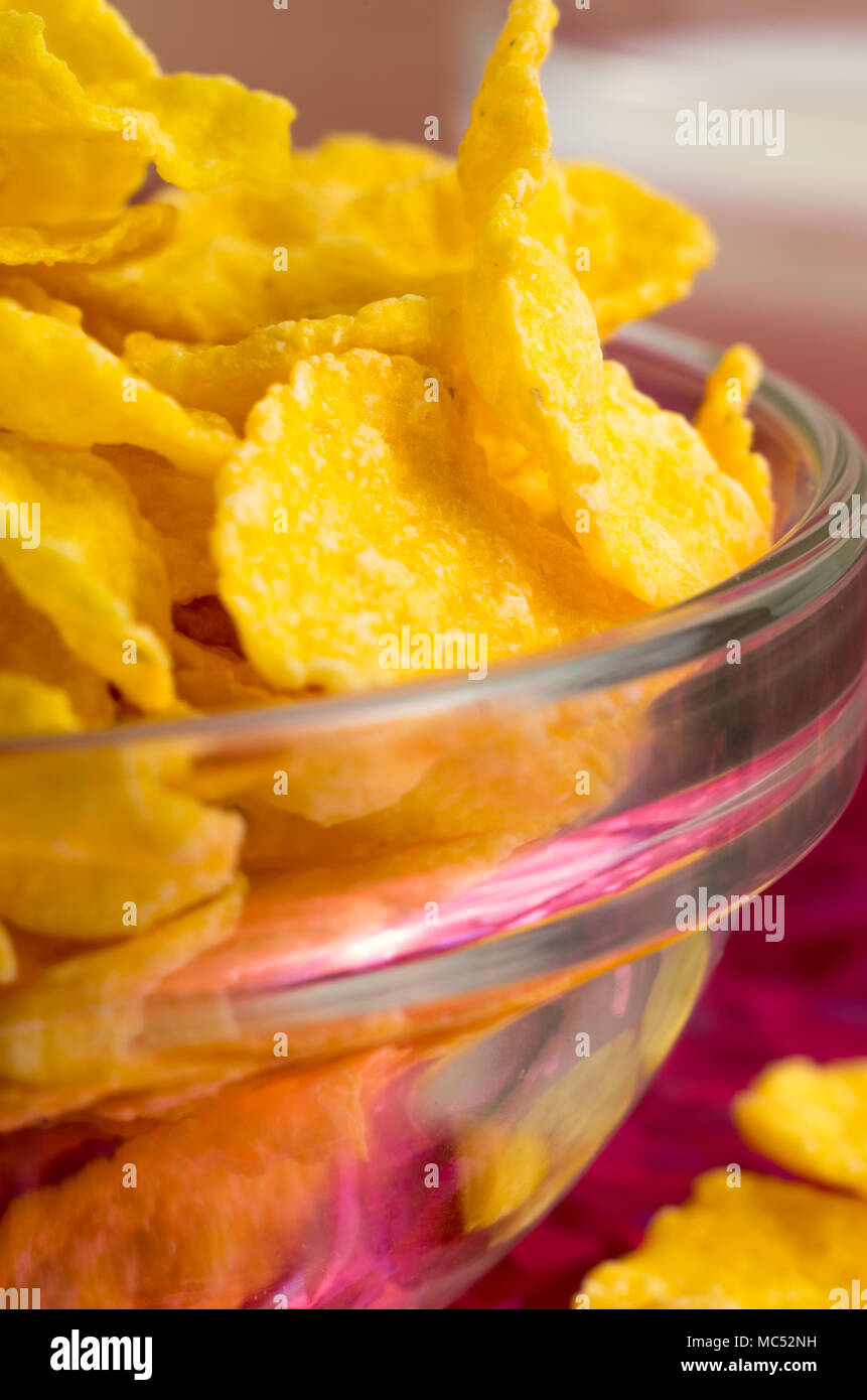 Ingredients for breakfast. Defocused and blurred macro view of yellow cornflakes in a transparent bowl closeup with shallow depth of focus Stock Photo