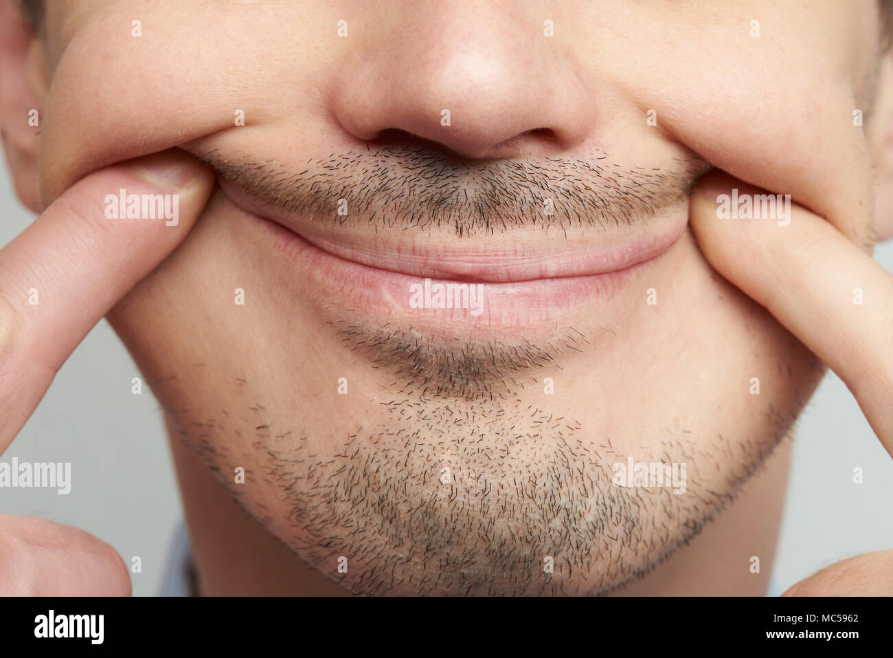 Forced fake smile close up on male face with beard Stock Photo