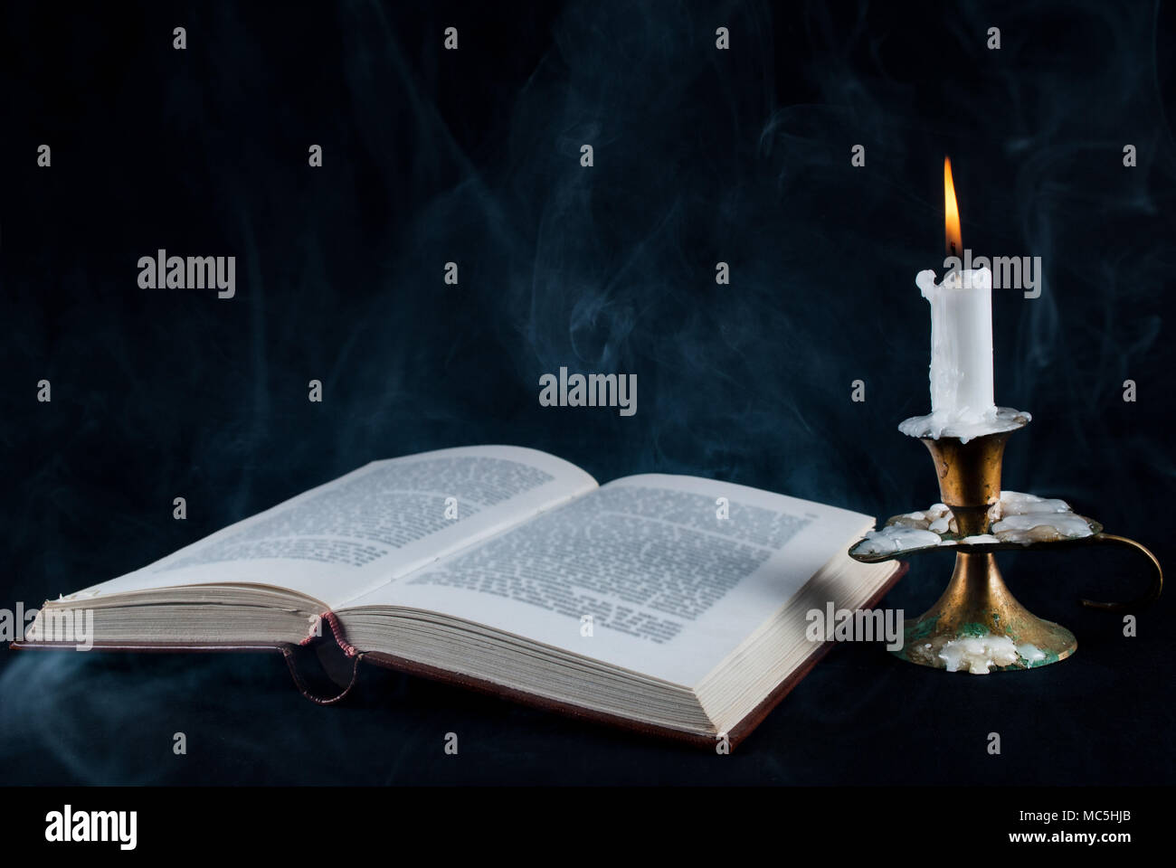 Old open book and candle in candlestick and smoke on dark black background  Stock Photo - Alamy